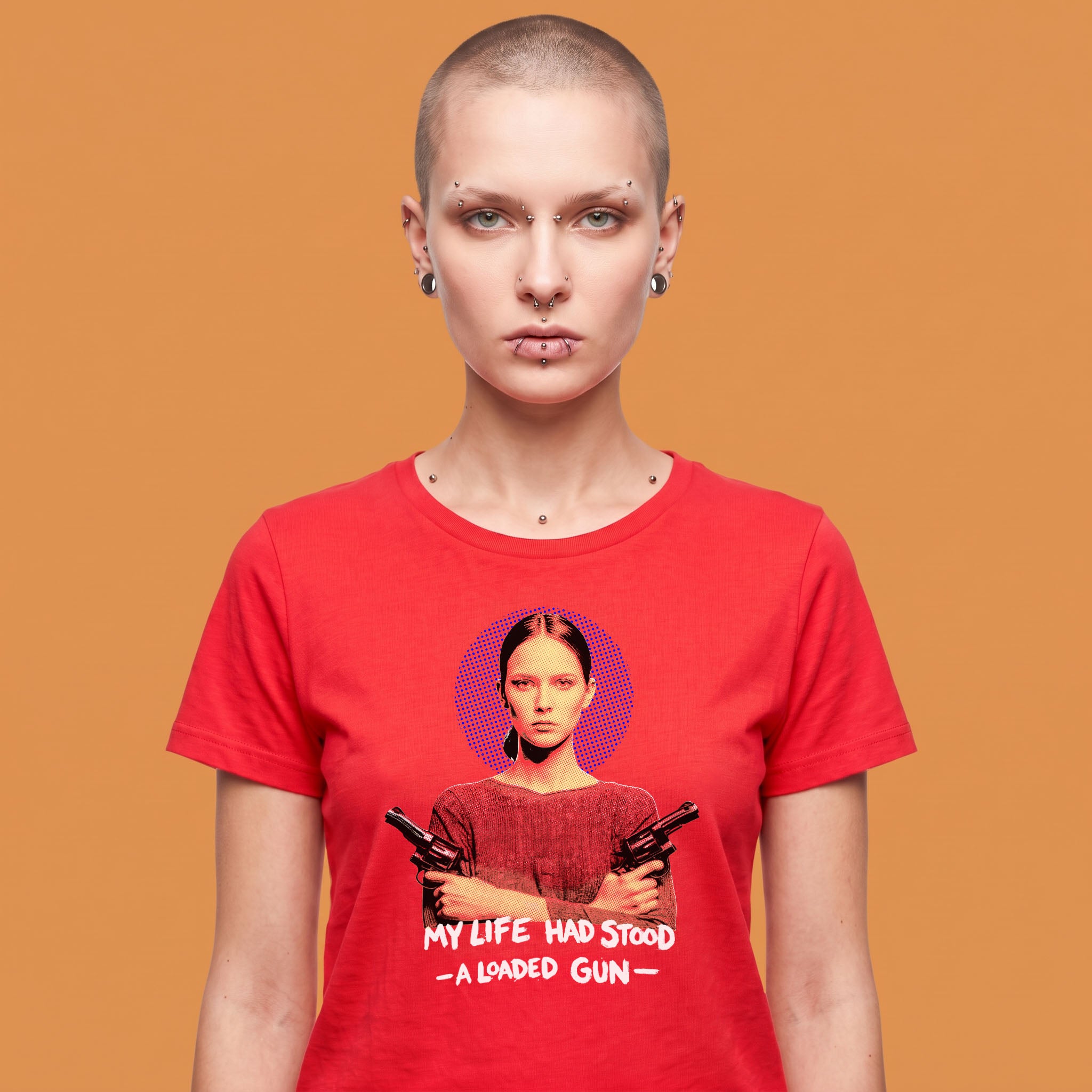 Camiseta de mujer de algodón orgánico rojo con ilustración gráfica de una mujer con dos armas y el texto My Life Had Stood A Loaded Gun en blanco, con detalle de QUADRA impreso en la manga izquierda