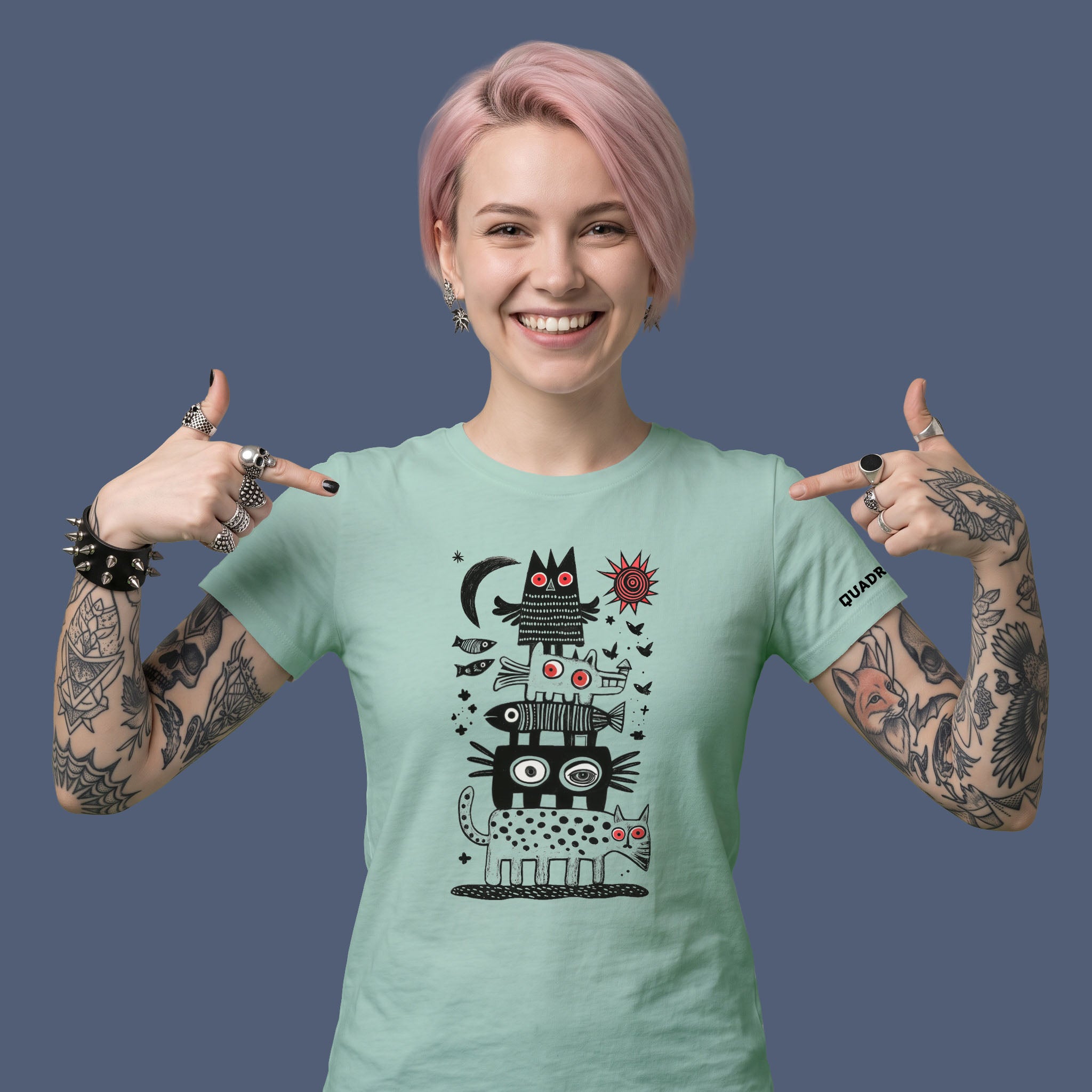 Woman wearing the NIGHT CITY aloe green unisex graphic T-shirt by QUADRA GALLERY, featuring stacked surreal animals beneath a moon and red sun.
